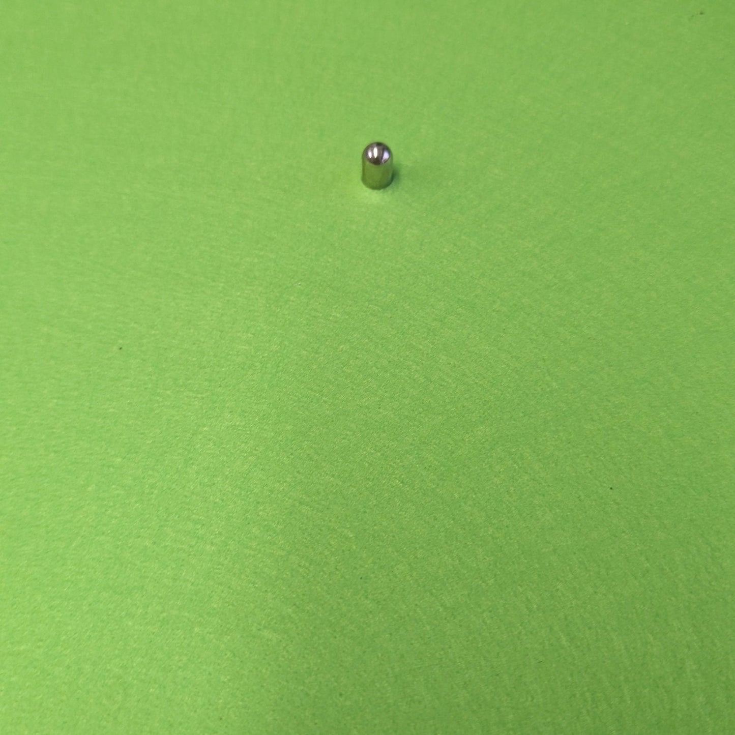 Green round object with a small metallic ball on top, placed on a flat surface.