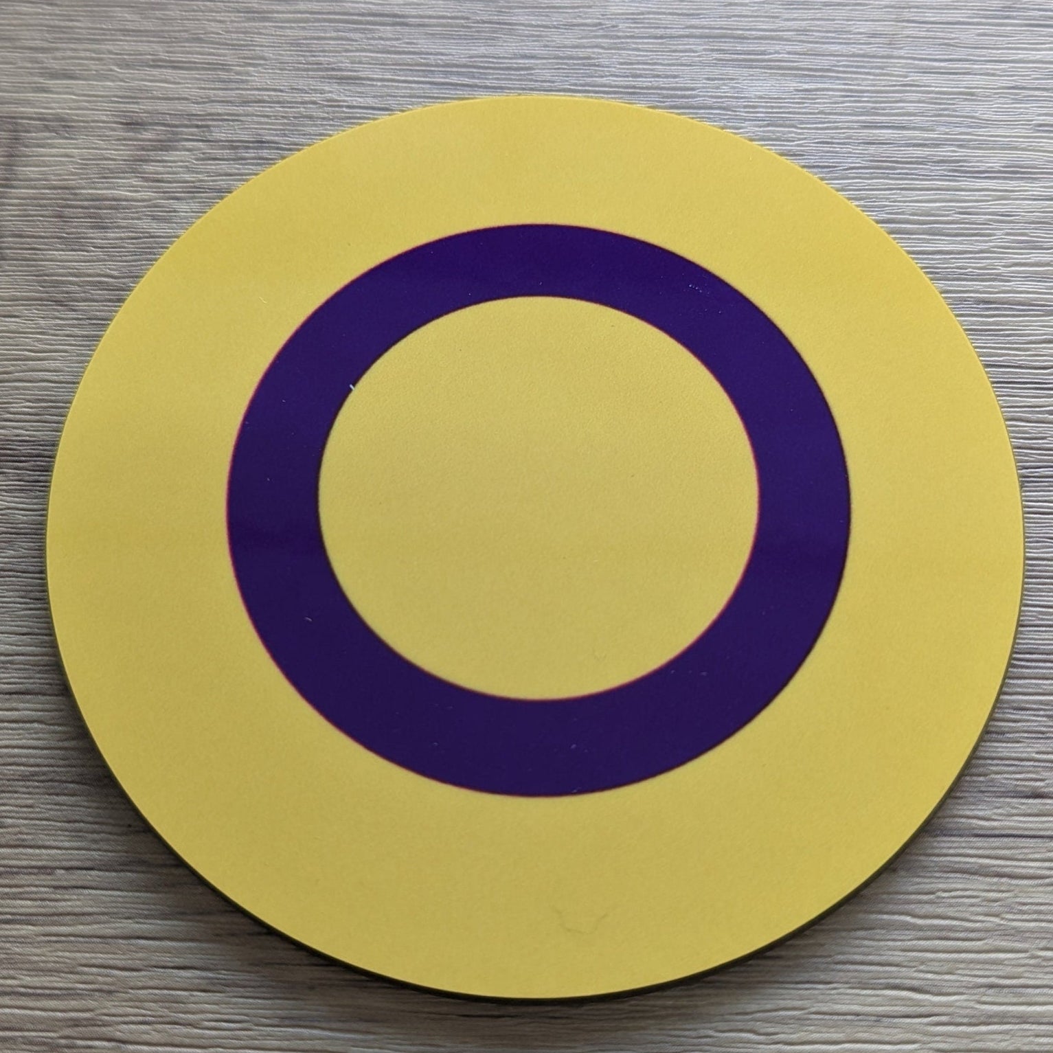 Intersex Pride Logo Yellow circle with a purple ring on a wooden surface