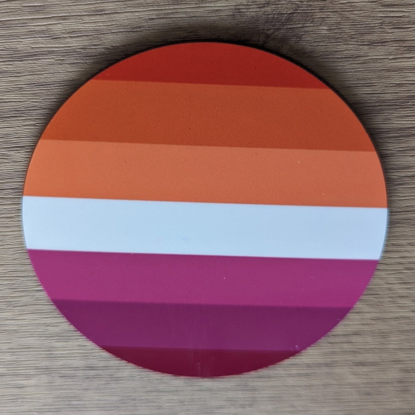 Round paper coaster with lesbian gay pride pattern on a wooden surface