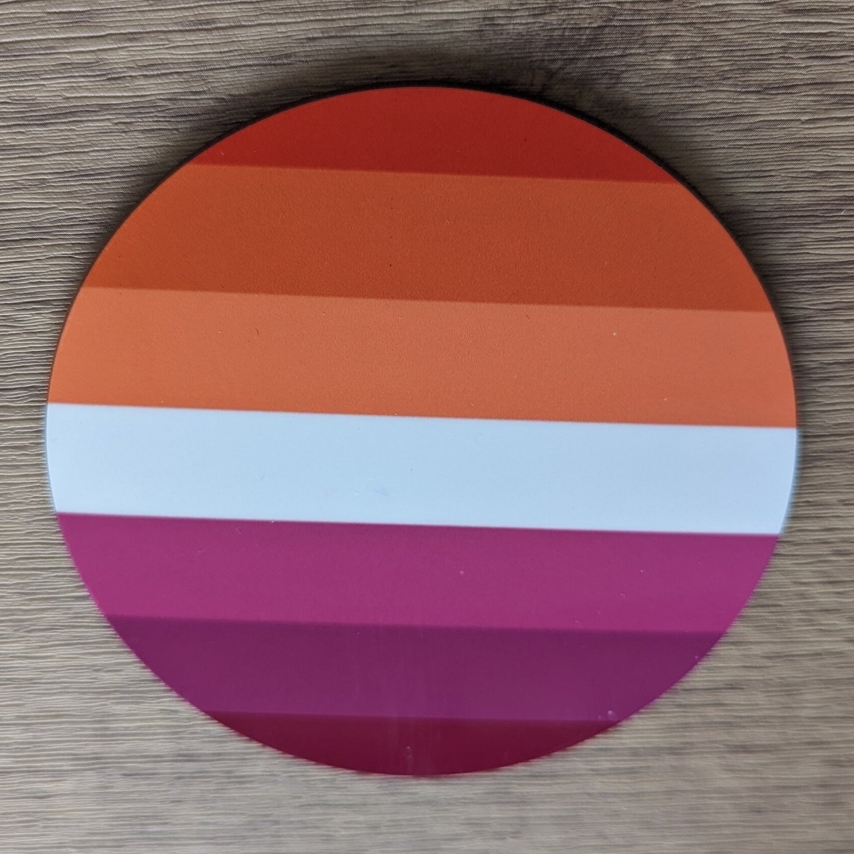 Round paper coaster with lesbian gay pride pattern on a wooden surface