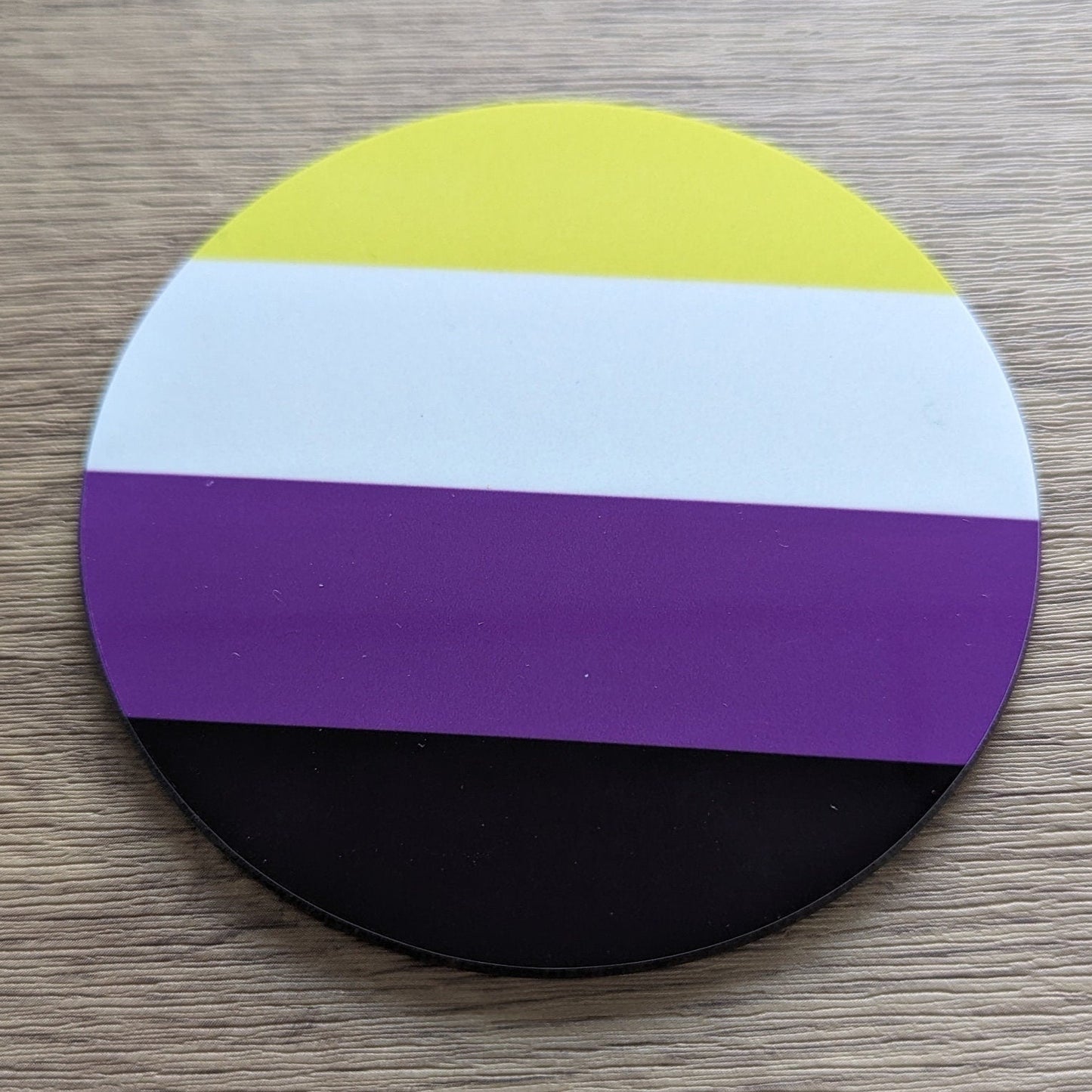 Round sticker with a non-binary pride flag on a wooden surface
