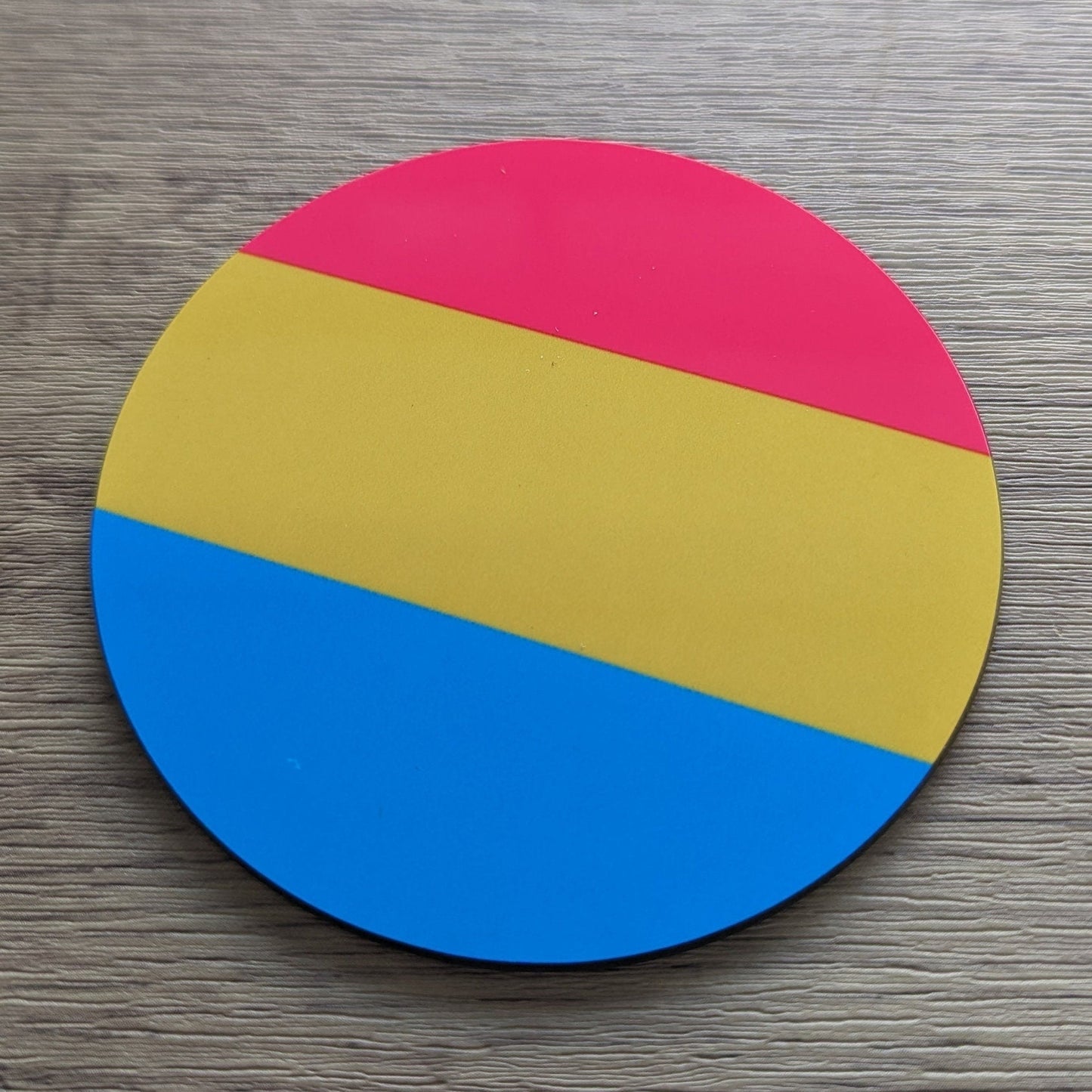 Round disc with pansexual pride pink, yellow, and blue sections on a wooden surface