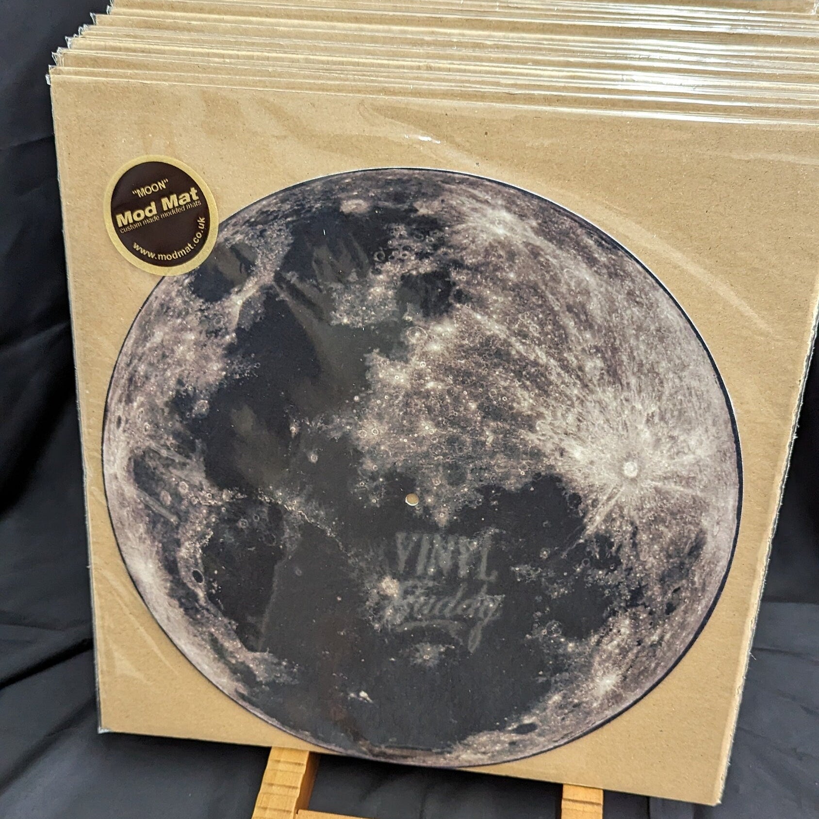 Vinyl record slipmat with moon design on a stand against a dark background