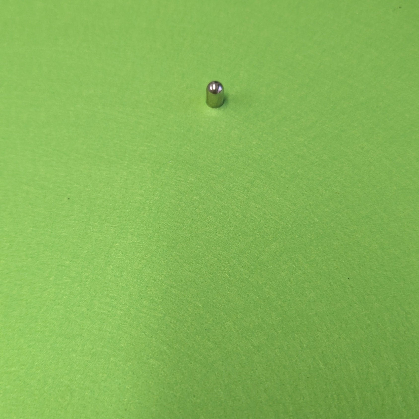 Green round object with a small metallic ball on top, placed on a flat surface.
