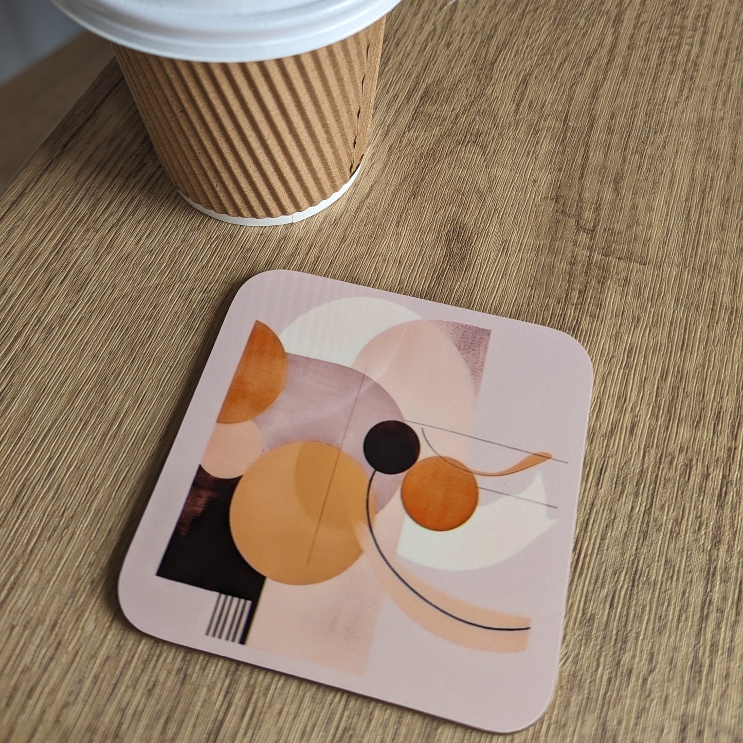 Coffee cup with a lid on a wooden surface next to a colorful coaster.