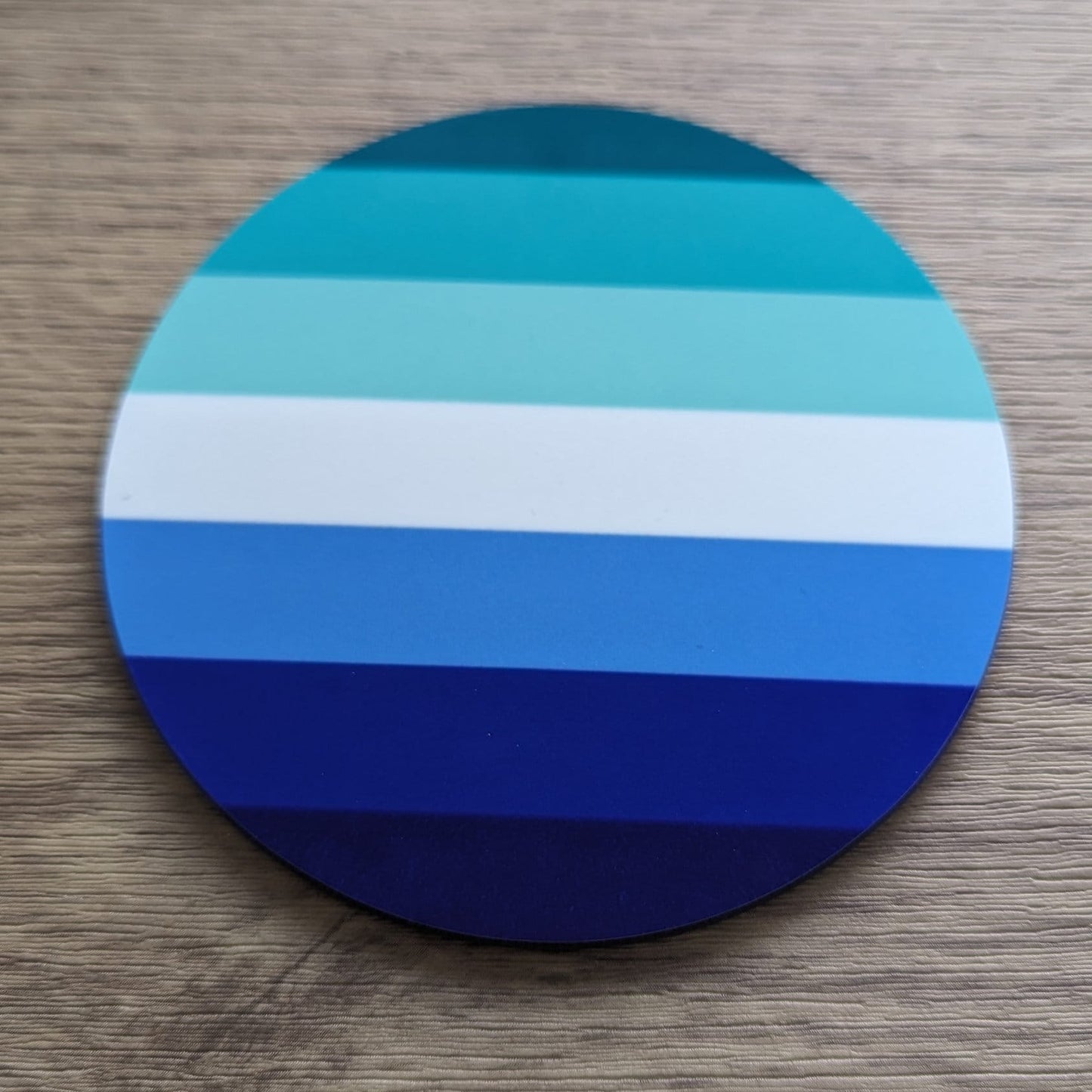 Round gay men blue and white striped coaster on a wooden surface