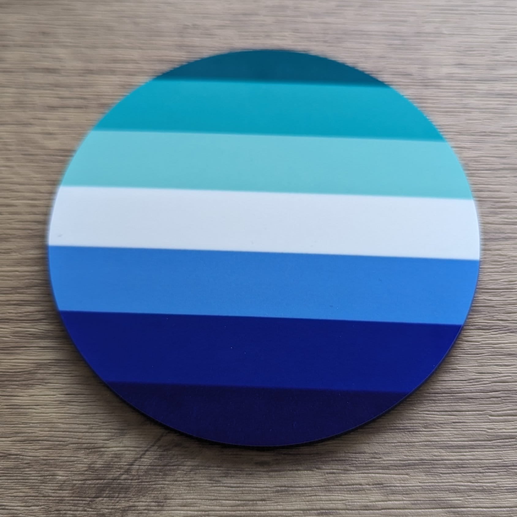 Round gay men blue and white striped coaster on a wooden surface